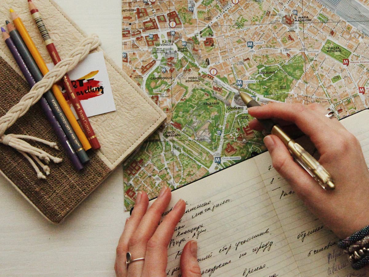 Hands writing travel notes over a city map, with pencils and glasses