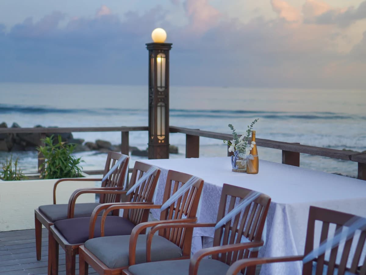 A dinner table set on a terrace by the ocean at dusk