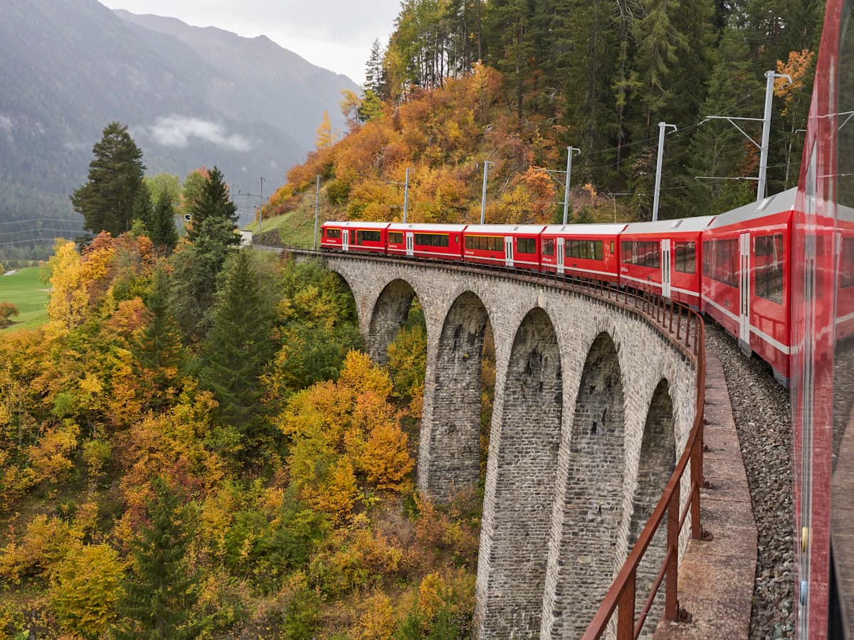 A red train crossing a stone viaduct through autumn forest in Switzerland